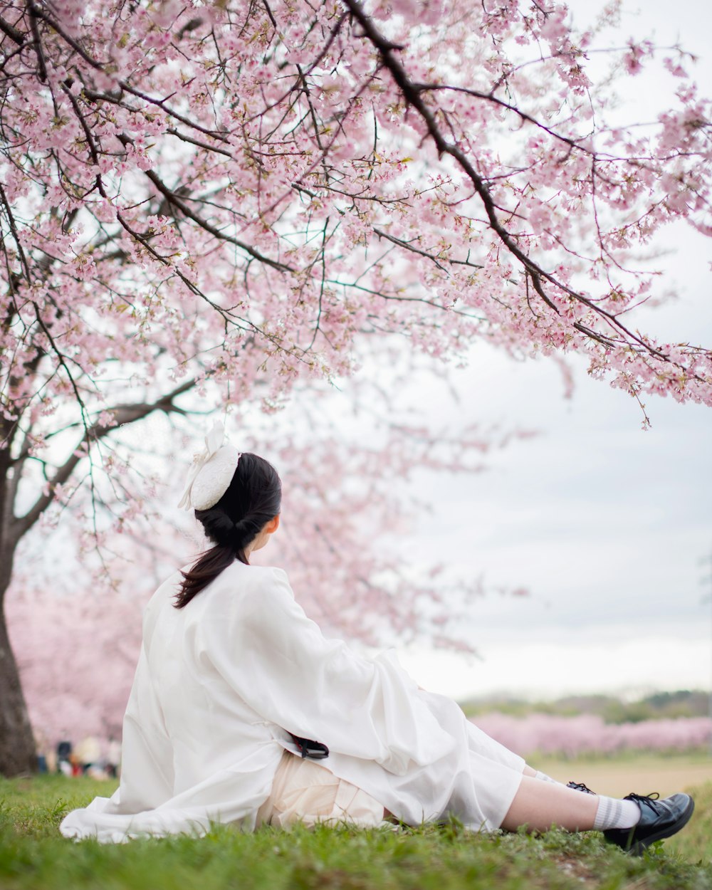 a woman sitting under a tree with pink flowers