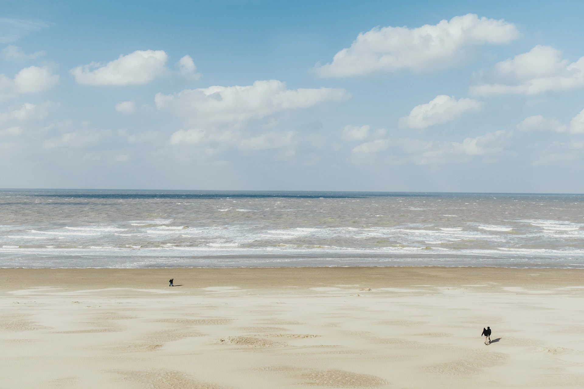 a couple of people walking across a sandy beach