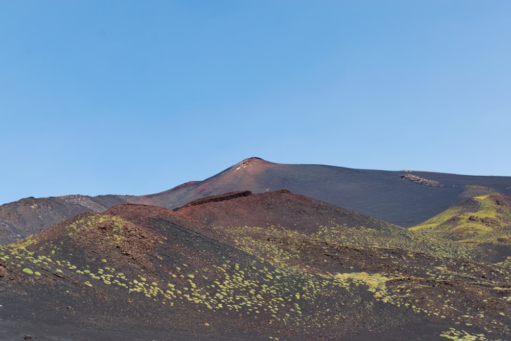 a mountain covered in grass and dirt under a blue sky