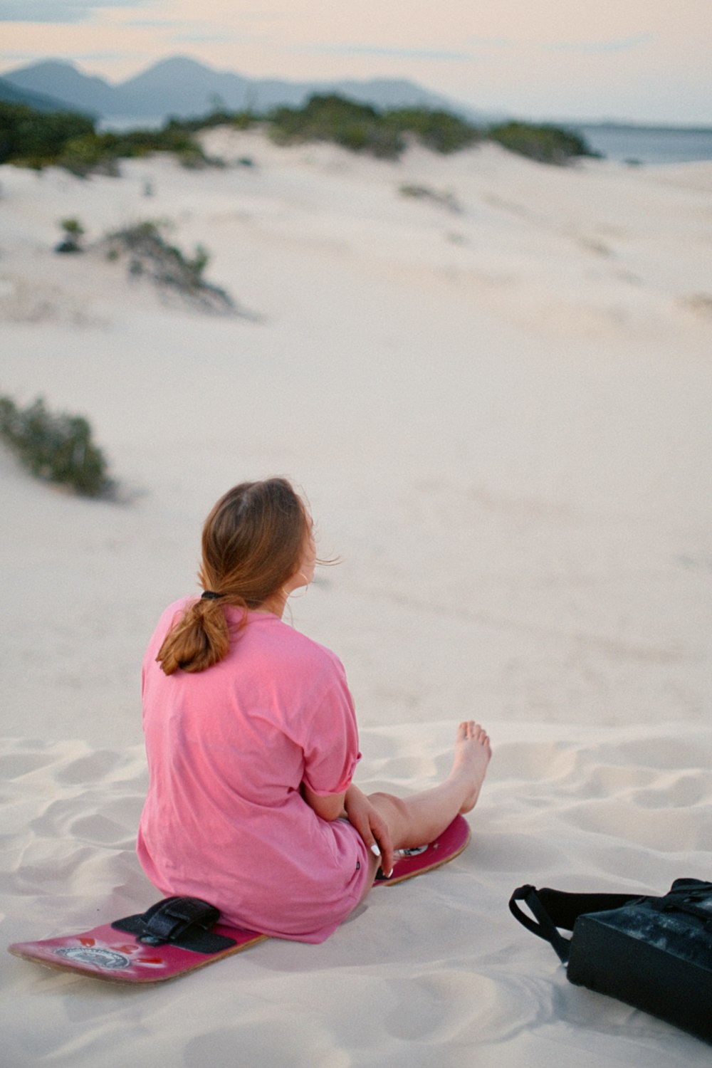 a woman sitting in the sand with a snowboard