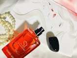 A red perfume bottle labeled 'Giorgio Armani Sì Passione éclat' is placed on a white surface next to a strand of pearls. In the background, a sophisticated sketch of a woman's face with bold red lipstick adds an artistic touch.