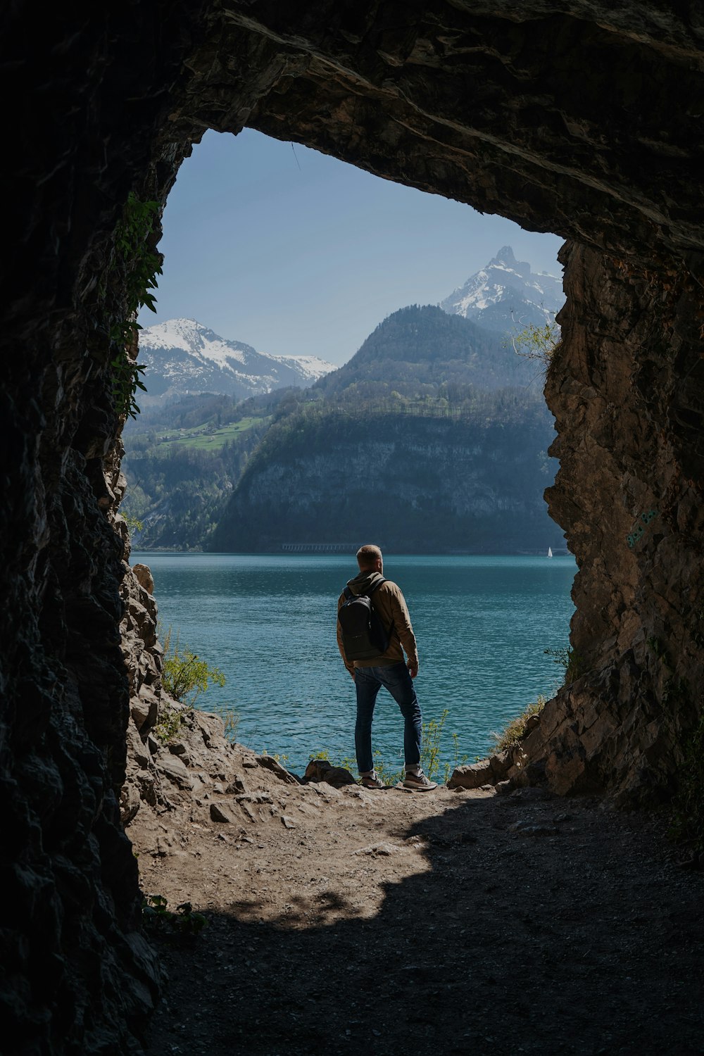 a man standing in a cave looking out at a lake