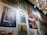 A wall gallery displaying various framed artworks, including a painting of a rustic building with a blue door, a vibrant abstract painting, a botanical print, and a market scene. The lighting is provided by a modern, spherical chandelier.