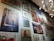 A wall gallery displaying various framed artworks, including a painting of a rustic building with a blue door, a vibrant abstract painting, a botanical print, and a market scene. The lighting is provided by a modern, spherical chandelier.