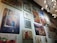 A wall gallery displaying various framed artworks, including a painting of a rustic building with a blue door, a vibrant abstract painting, a botanical print, and a market scene. The lighting is provided by a modern, spherical chandelier.