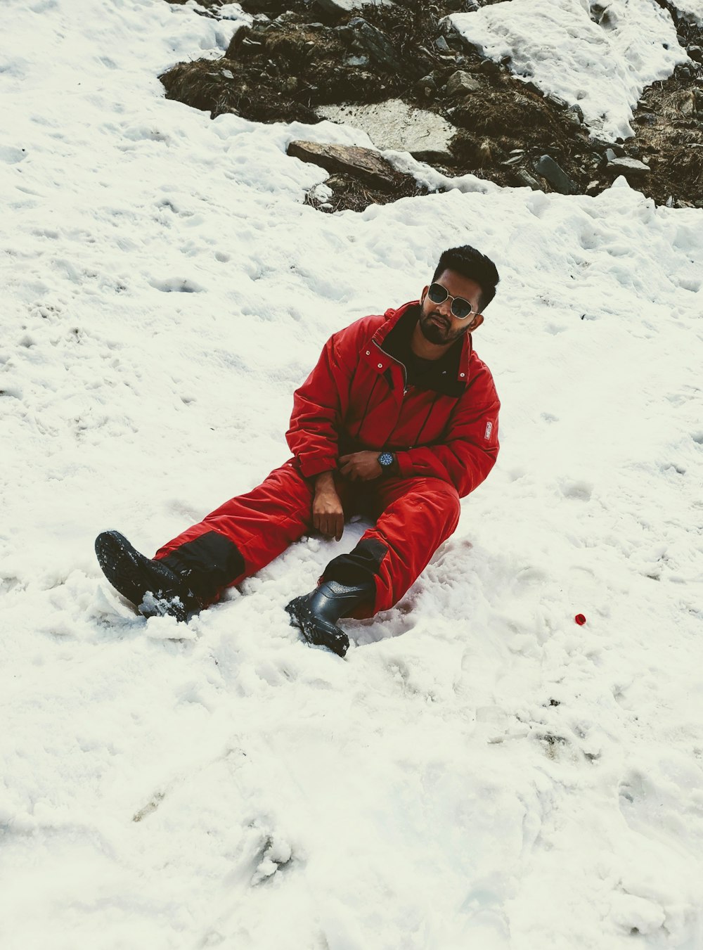 a man in a red snow suit sitting in the snow