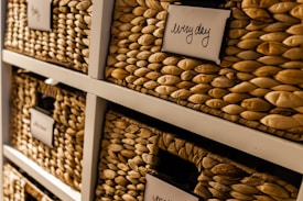 Woven baskets are neatly arranged on shelves with labels attached to them. The baskets have a natural, textured appearance and the labels are written in a cursive style.