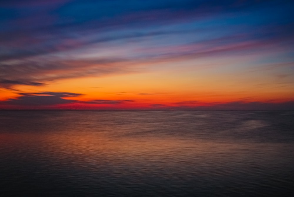 a beautiful sunset over the ocean with clouds in the sky