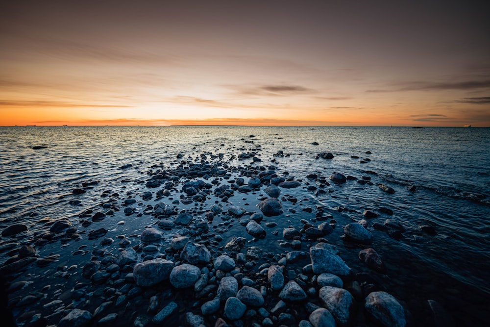 a sunset over a body of water with rocks in the foreground