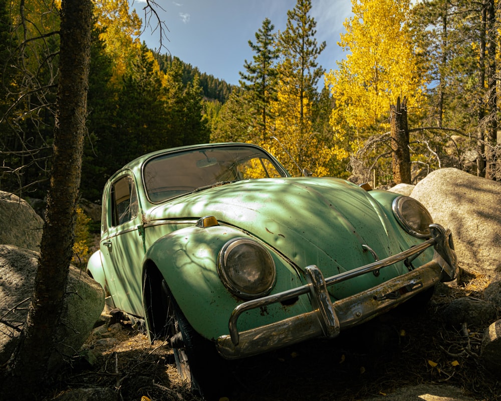 an old green car is parked in the woods