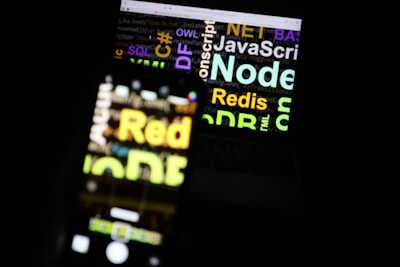 A blurred image showing a laptop screen with various programming-related words such as 'Node', 'JavaScript', 'Redis', and 'SQL'. The text appears in different colors and sizes, overlaid on the screen.