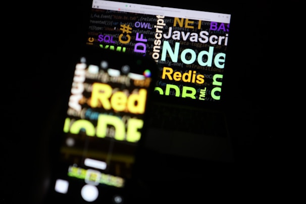A blurred image showing a laptop screen with various programming-related words such as 'Node', 'JavaScript', 'Redis', and 'SQL'. The text appears in different colors and sizes, overlaid on the screen.