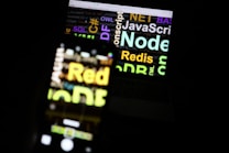 A blurred image showing a laptop screen with various programming-related words such as 'Node', 'JavaScript', 'Redis', and 'SQL'. The text appears in different colors and sizes, overlaid on the screen.
