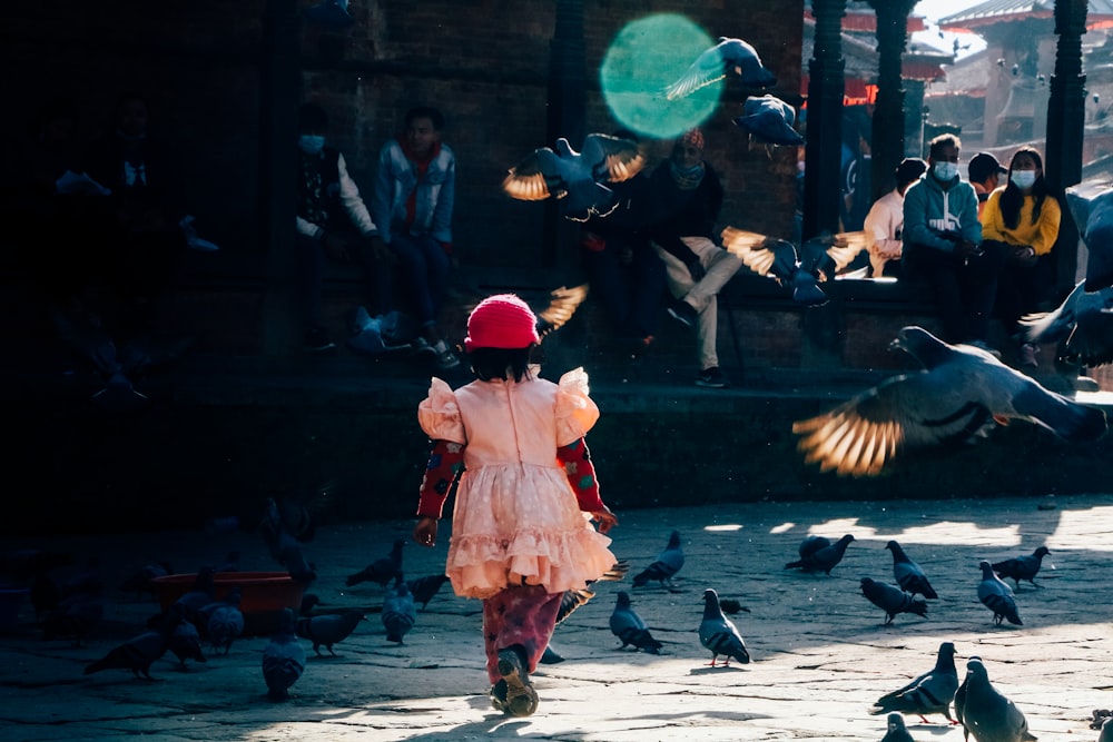 a little girl in a pink dress and a bunch of pigeons