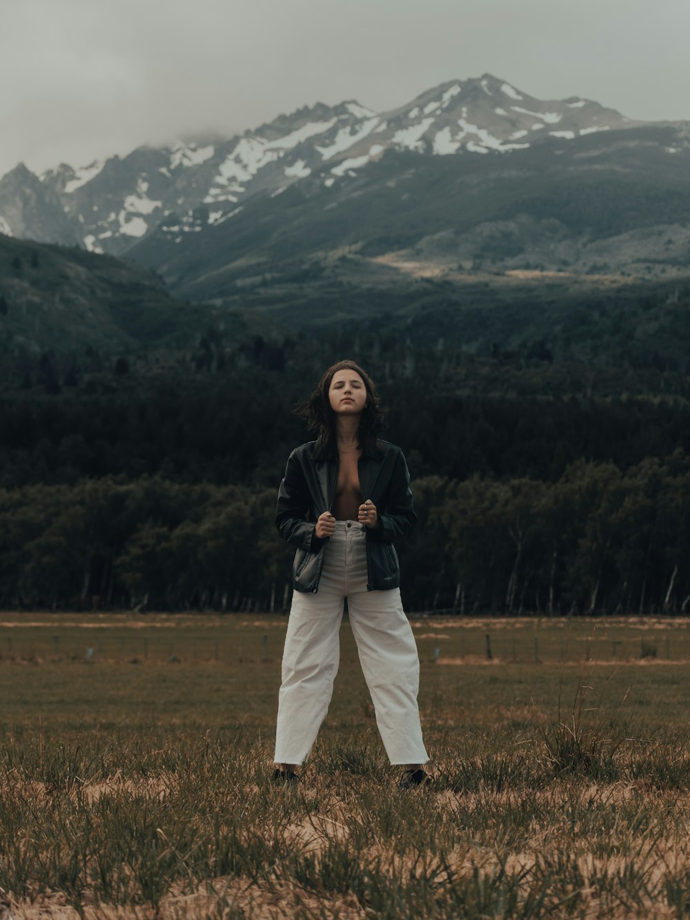 a woman standing in a field with mountains in the background