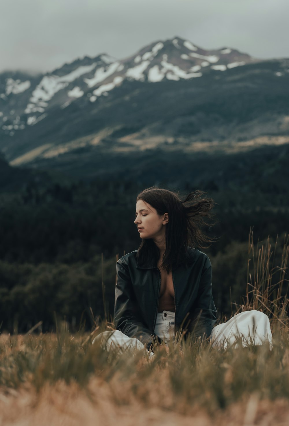 a woman sitting in a field with mountains in the background