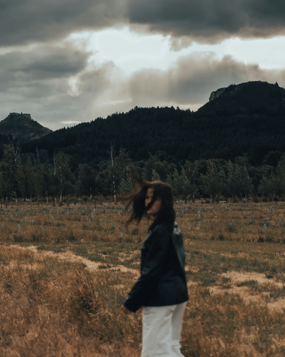 a woman walking through a field with a mountain in the background