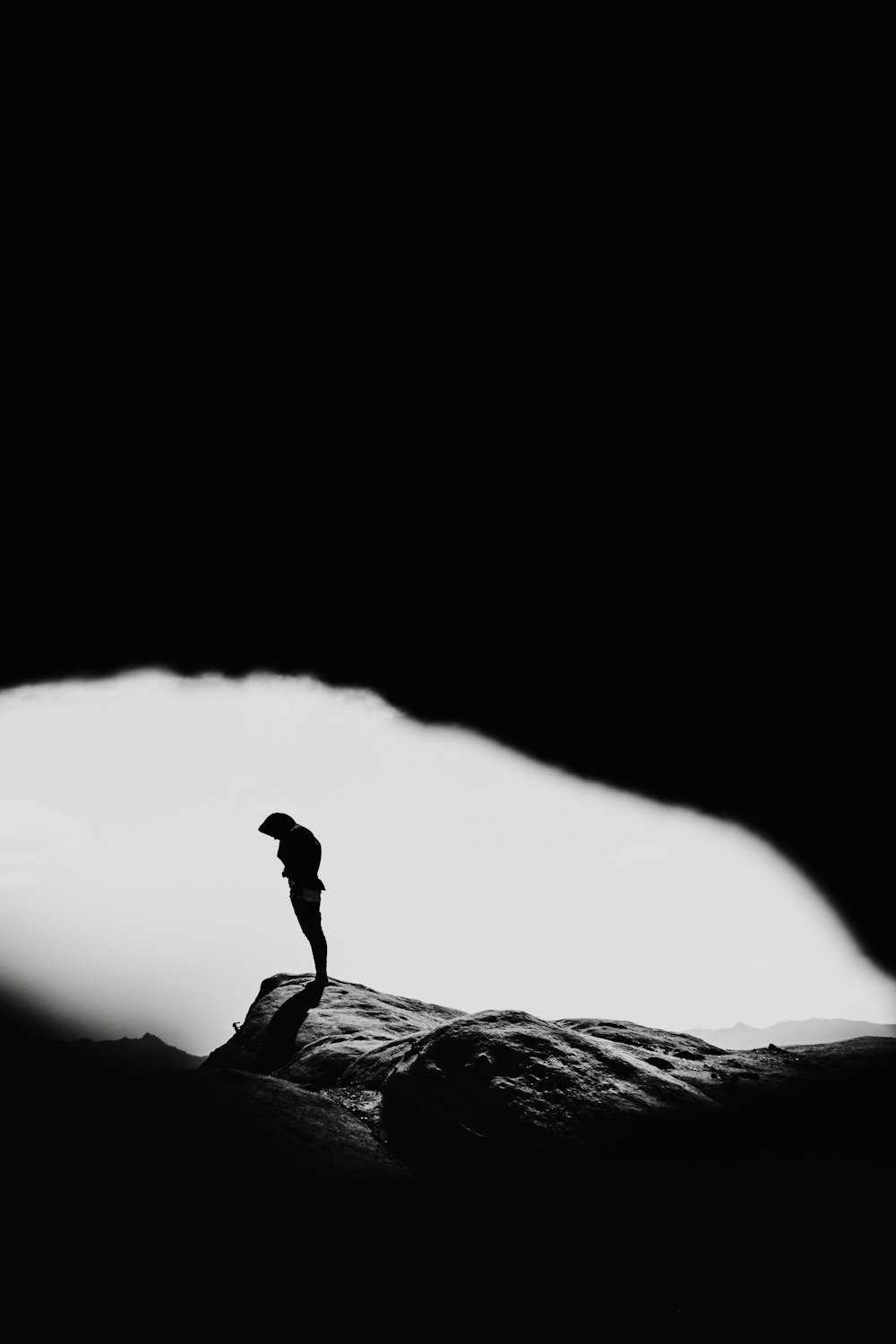 a black and white photo of a person standing on a rock