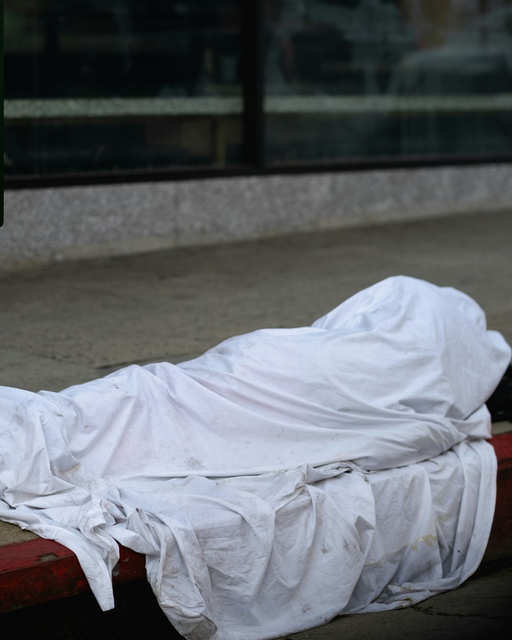 a white sheet is covering a man's body on a red bench