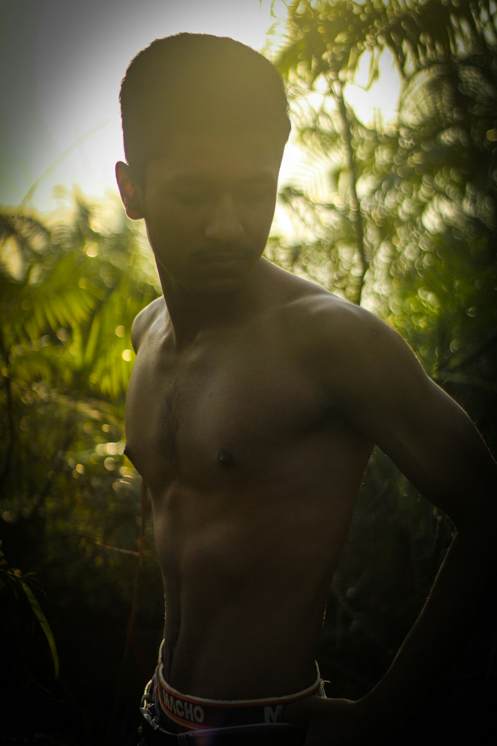 a man with no shirt standing in a forest