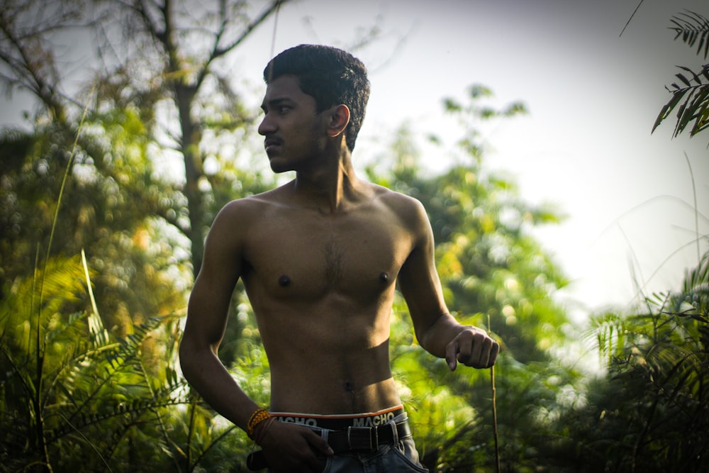 a man without a shirt standing in a forest
