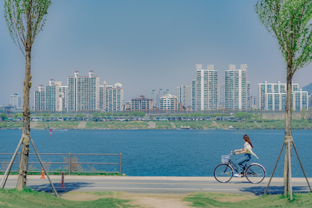 a woman riding a bike down a street next to a lake