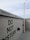 A concrete wall featuring multiple 'Do Not Disturb' signs in bold black letters. A security camera is mounted on a pole extending from the ground, and the sky above is overcast with light gray clouds.