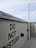 A concrete wall featuring multiple 'Do Not Disturb' signs in bold black letters. A security camera is mounted on a pole extending from the ground, and the sky above is overcast with light gray clouds.