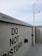 A concrete wall featuring multiple 'Do Not Disturb' signs in bold black letters. A security camera is mounted on a pole extending from the ground, and the sky above is overcast with light gray clouds.