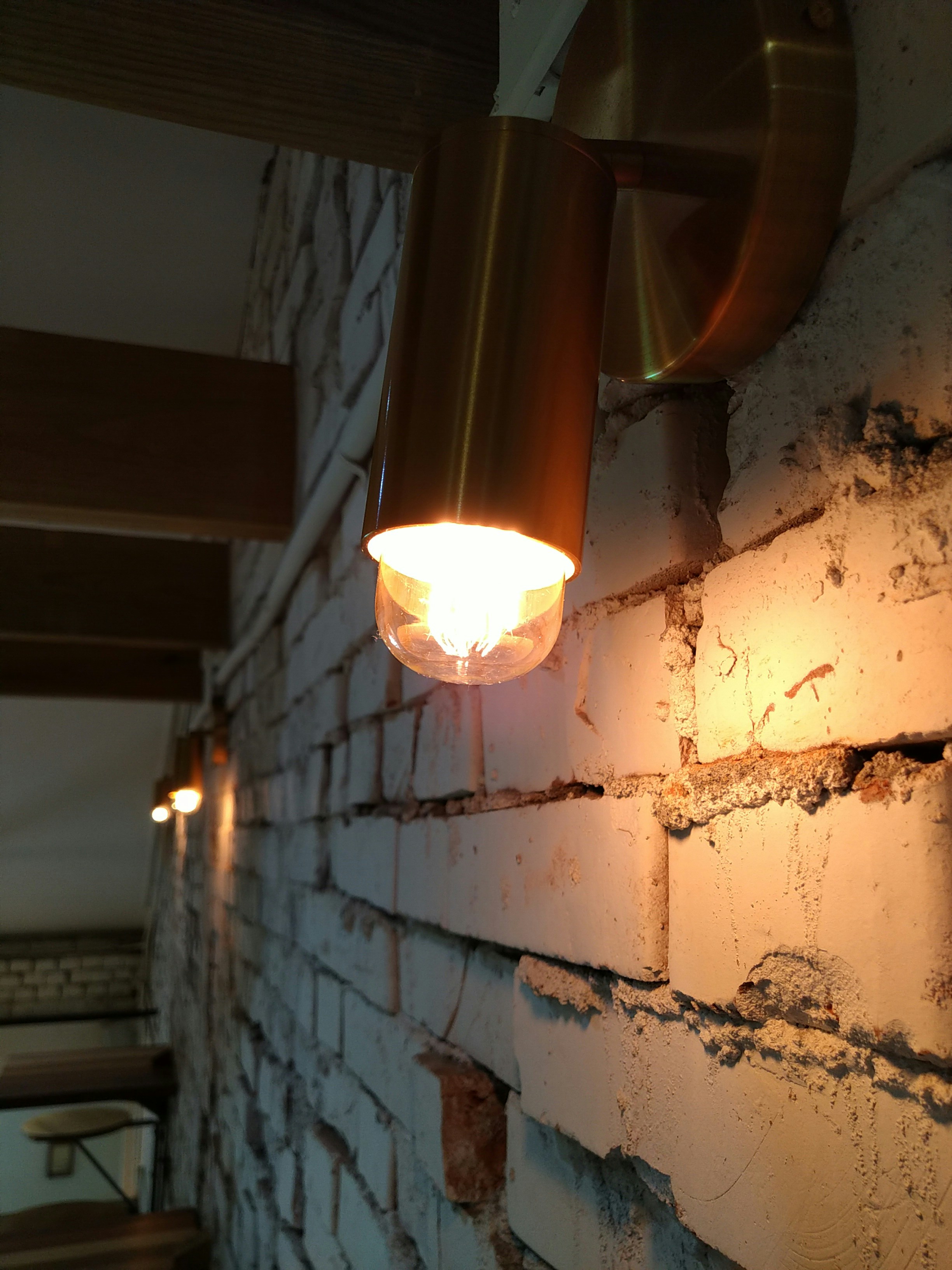 Architectural brass wall sconce casting a warm directional glow on textured plaster wall in a luxury hallway