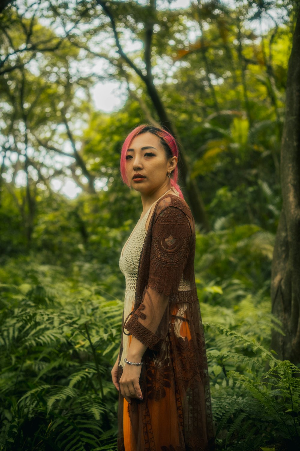 a woman with pink hair standing in a forest