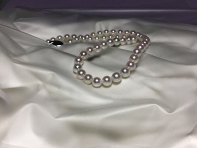 A strand of pearls is elegantly arranged on a smooth, satin-like surface, displaying their luster and reflecting light softly. The pearls are evenly sized and have a classic round shape, enhancing their timeless appeal.