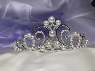 A delicate bridal tiara sparkling with crystals, resting on soft white silk fabric.