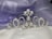 A luxurious silver tiara adorned with pearls and small diamonds rests on a soft, silky fabric backdrop in shades of lavender and white. The tiara features intricate scrollwork with a symmetrical design, combining elegance and regal sophistication.