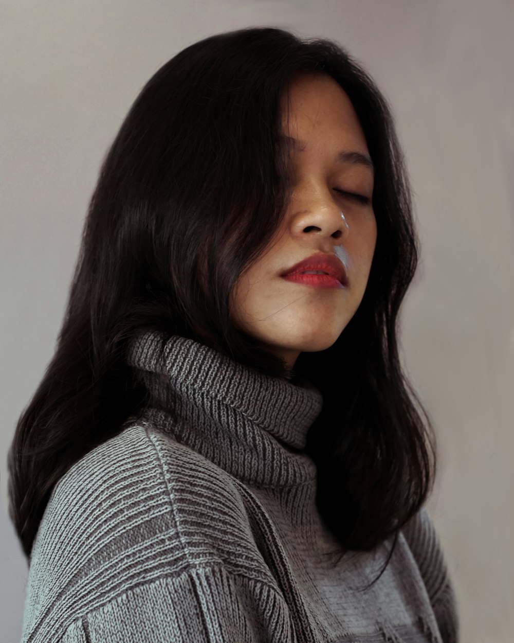 a woman with her eyes closed wearing a gray sweater