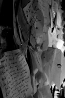 A collection of handwritten notes attached to a surface, with overlapping layers creating a textured effect. The notes contain various texts in different handwriting styles, evoking a sense of collective storytelling or shared experiences.