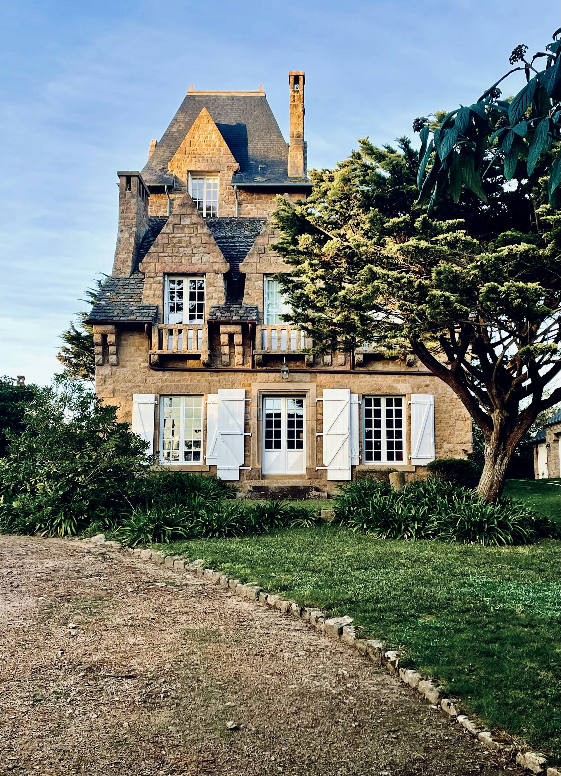 Elegant stone country house with a cozy porch and blooming flowers in the garden.