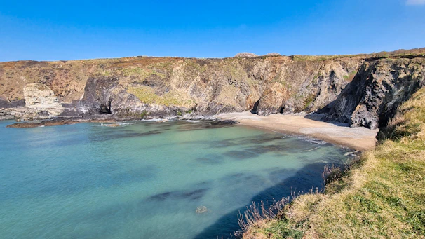 A quiet cove where clear blue water meets smooth pebbles under a bright sky.