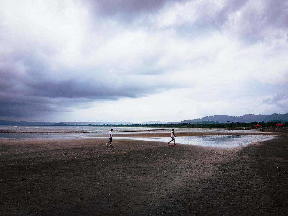 a couple of people standing on top of a sandy beach