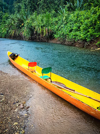 a yellow canoe sitting on the side of a river