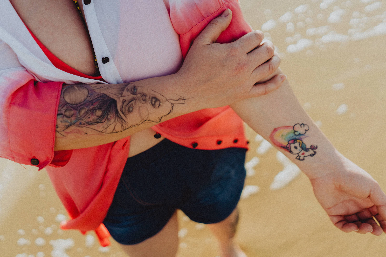 Tattooed arms in bright daylight with a coral-red shirt.