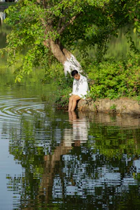 A young man sitting peacefully by a lake at sunrise, reflecting deeply.