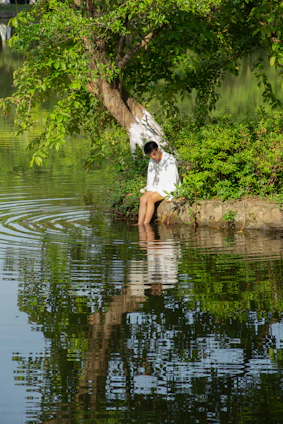 A serene scene of a person sitting peacefully by a lake at sunset, surrounded by soft greenery.