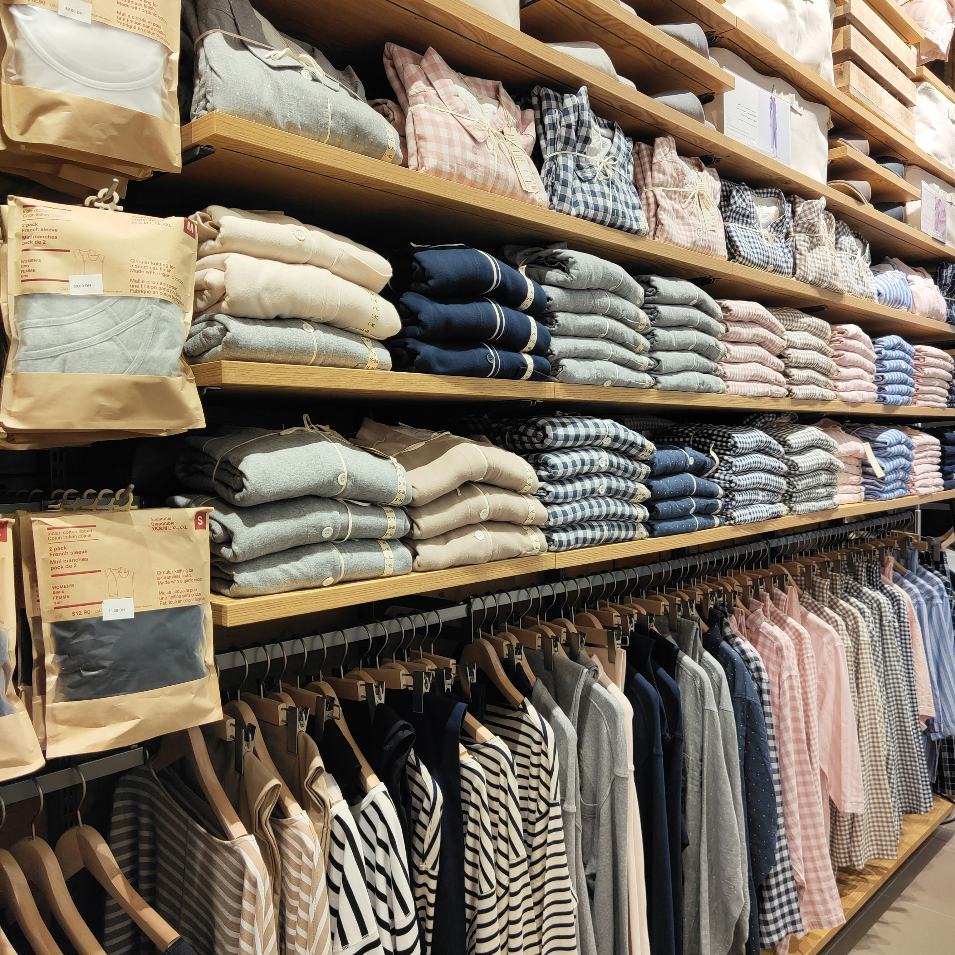 Neatly folded white linen shirts stacked on a wooden shelf against a white wall