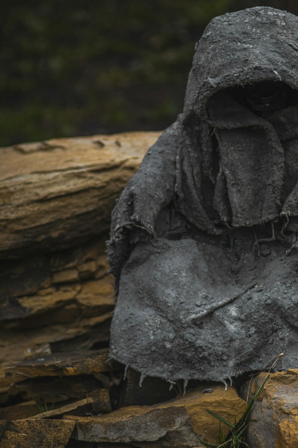 a statue of a person with a hood on sitting on some rocks