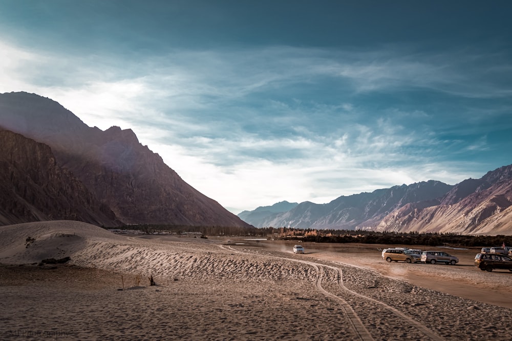 a group of cars parked in a desert with mountains in the background