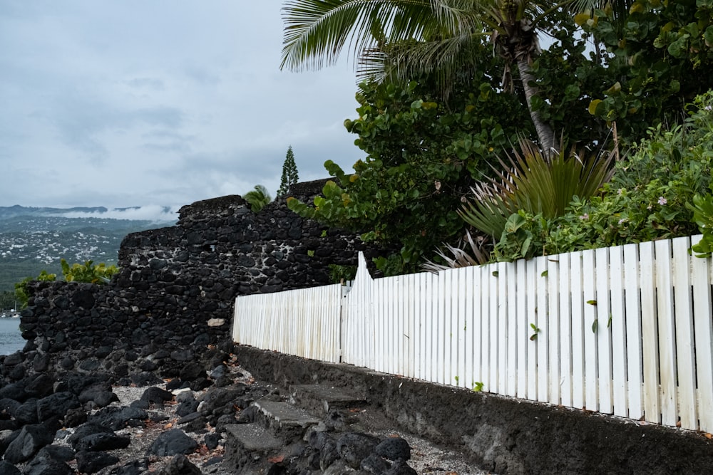 a white picket fence next to a lush green hillside