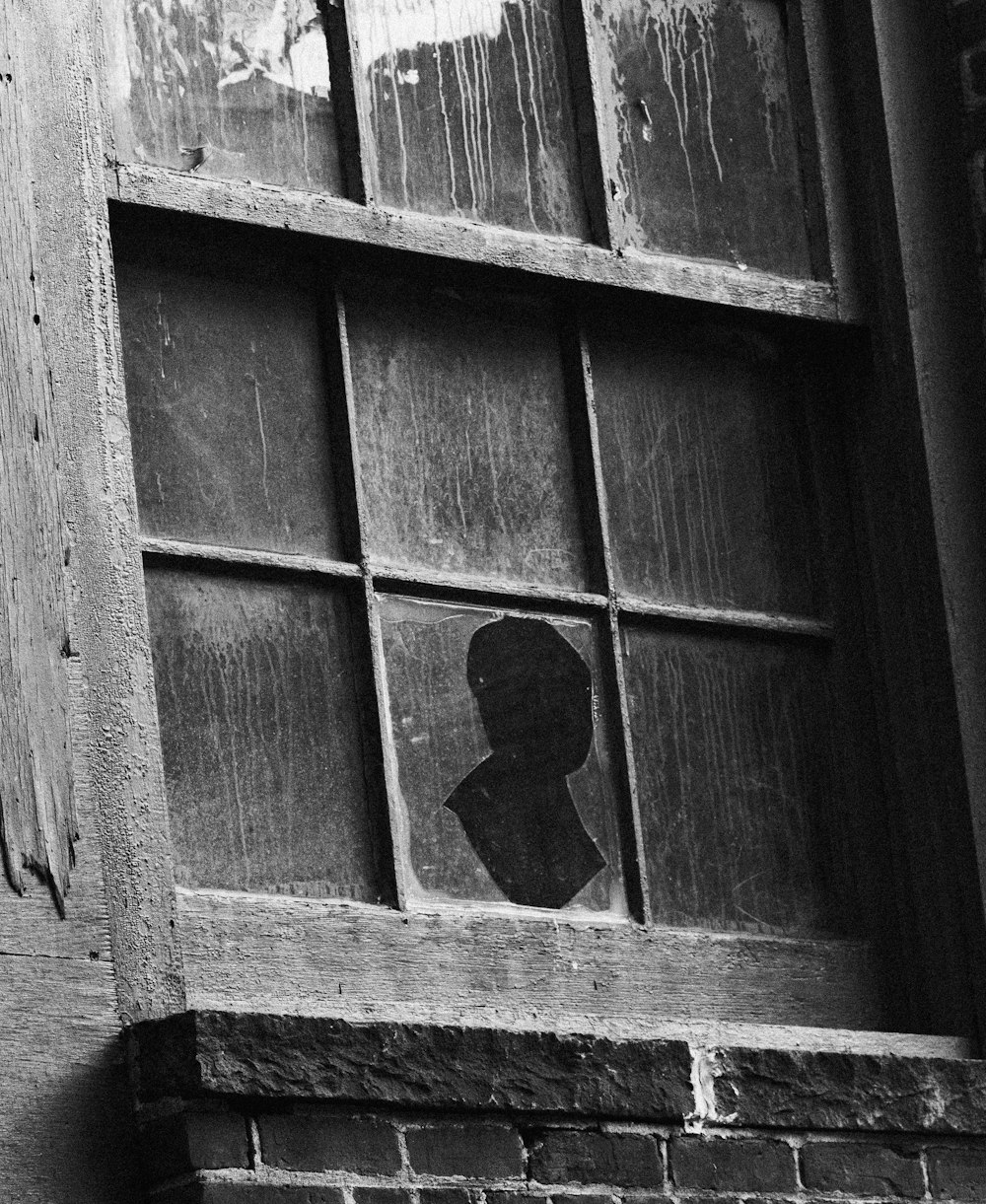 a black and white photo of a window with a shadow of a person