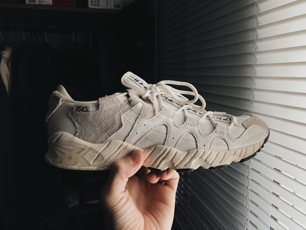 a person holding up a white sneaker in front of a window