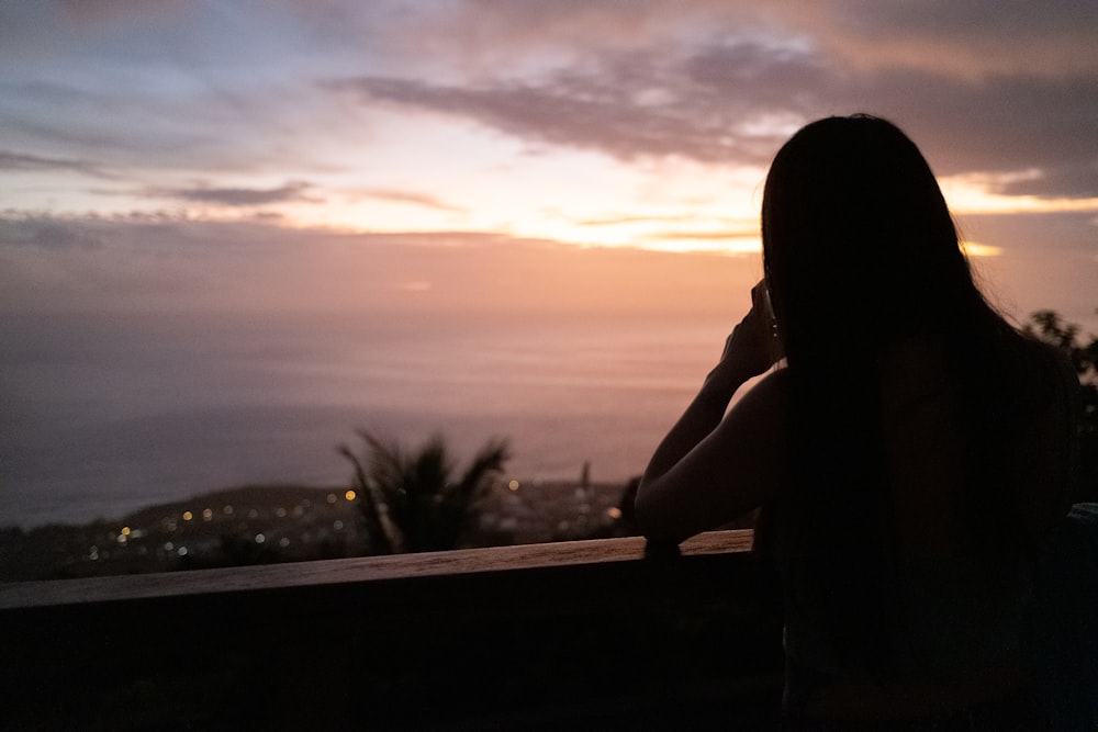 a woman sitting on a balcony watching the sunset